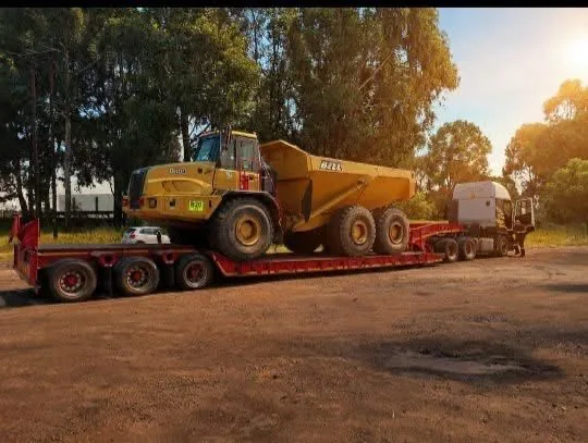 A Bell articulated dump truck loaded onto a lowbed trailer at golden hour