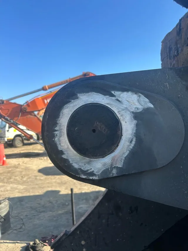 A boom eye with fresh weld metal deposited around the worn bore, photographed outdoors against a blue sky