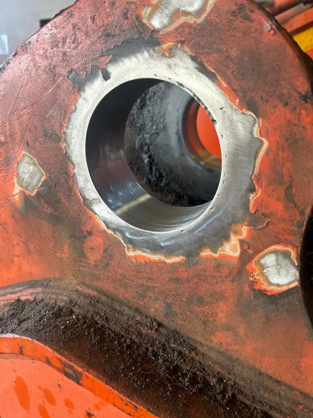 Ring of weld build-up inside a bore on an orange machine casting, waiting to be cut back to size