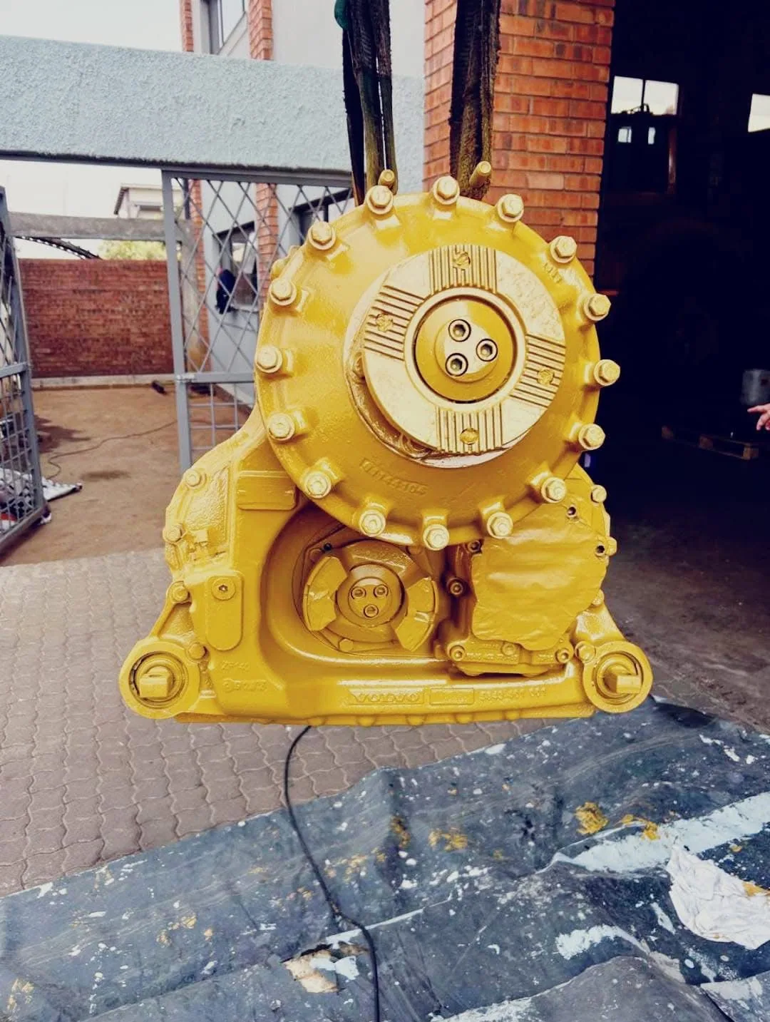 A rebuilt final drive assembly painted yellow, lifted on slings outside the workshop