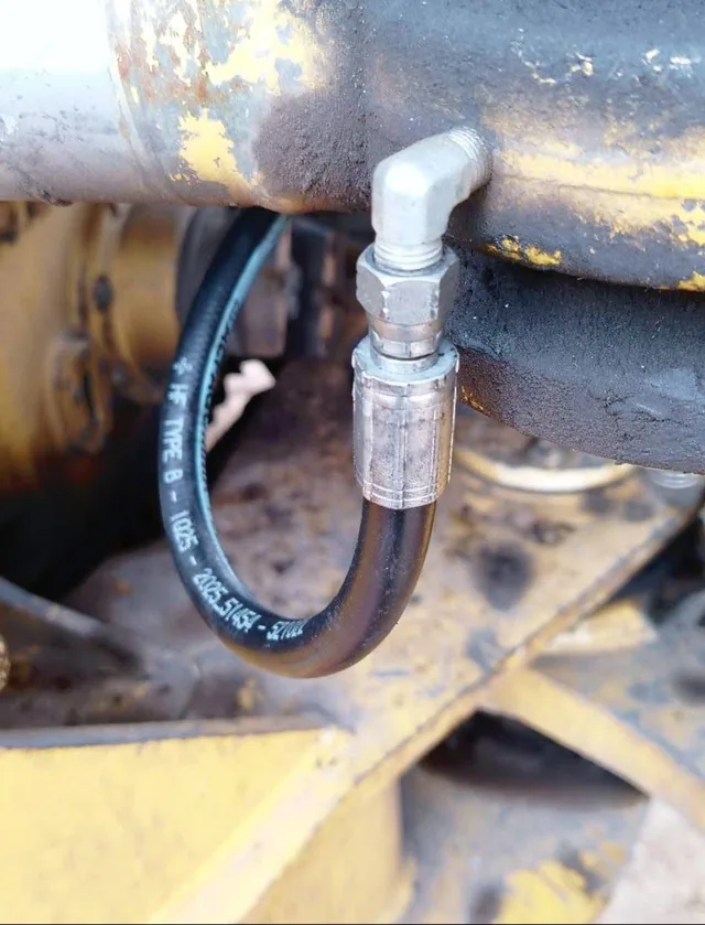 A newly crimped hydraulic hose fitted to an elbow union on yellow plant machinery