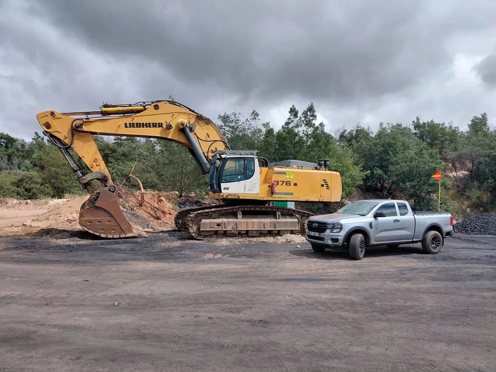 A Liebherr R976 tracked excavator parked beside a service vehicle on a haul road