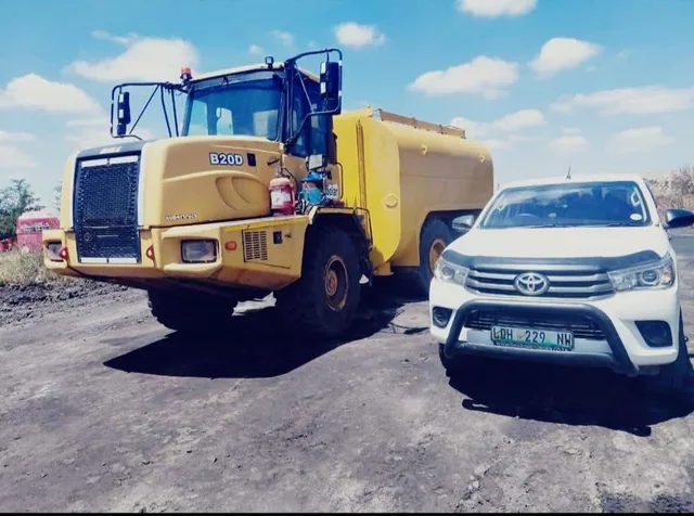 An articulated water bowser truck parked beside a service vehicle on a haul road